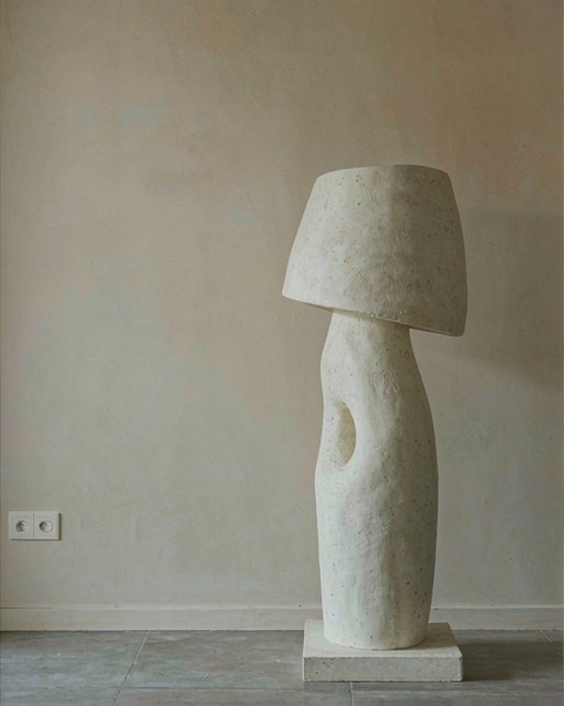 A plaster floor lamp on a low plinth in a plaster-walled studio